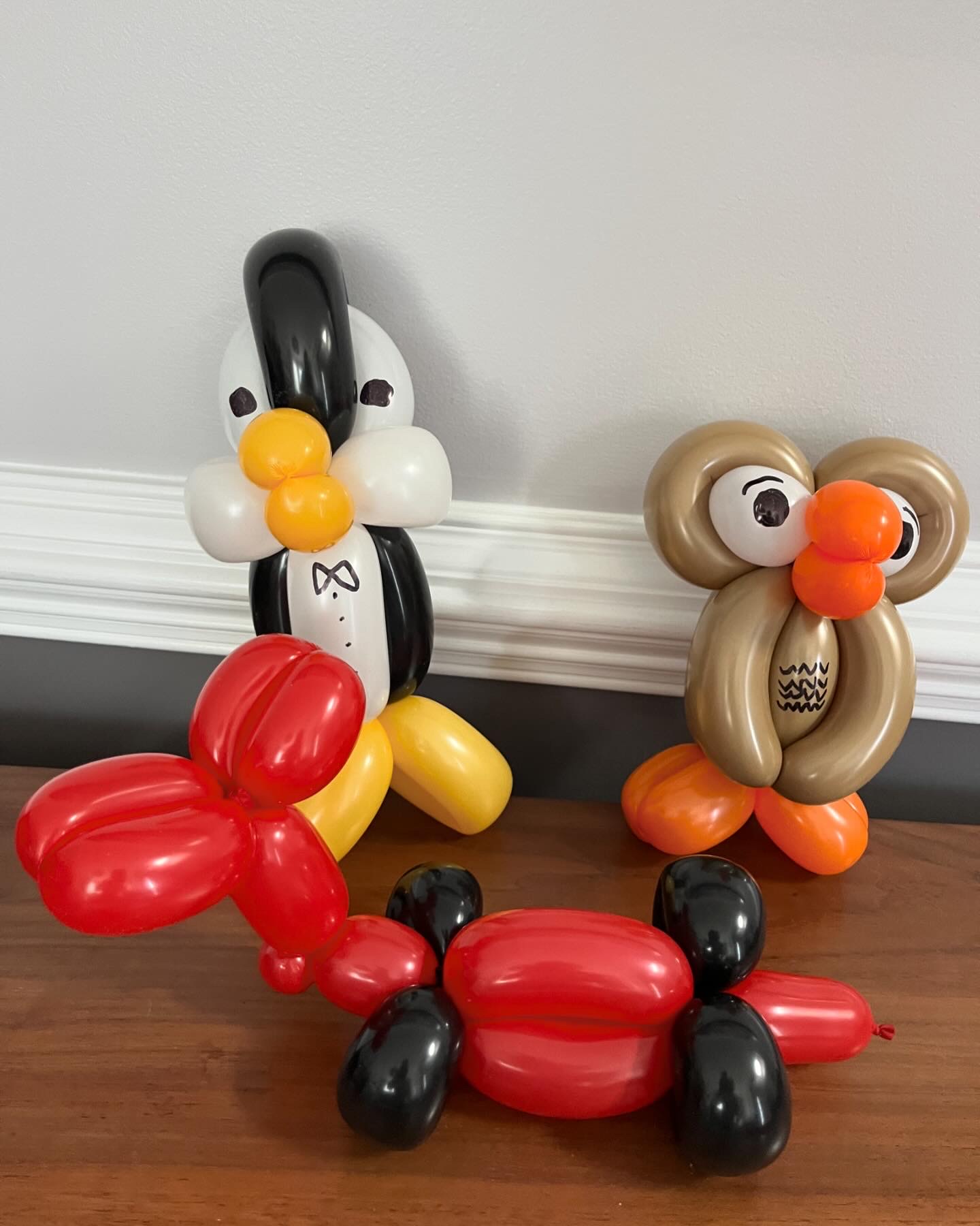 Balloon penguin in a tuxedo, a red balloon dog, and a gold owl